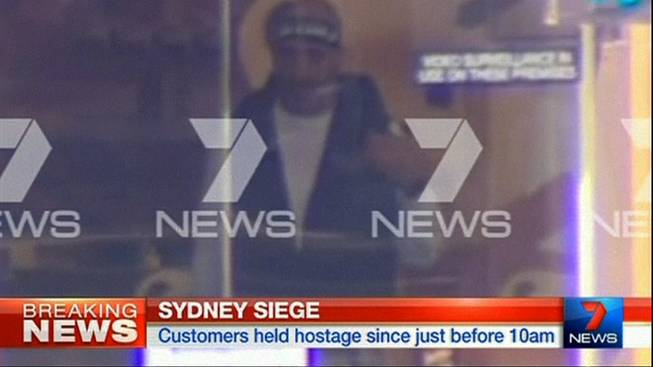 This image taken from video shows a man believed to be a gunman inside a cafe in Sydney, Australia Monday, Dec. 15, 2014. An apparent hostage situation was unfolding inside the chocolate shop and cafe in Australia's largest city on Monday, where several people could be seen through a window with their hands held in the air. 