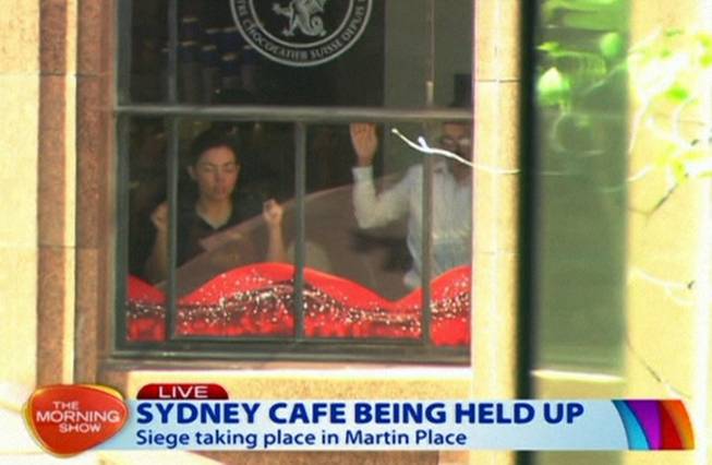 This image taken from video shows people holding up hands inside a cafe in Sydney, Australia Monday, Dec. 15, 2014. An apparent hostage situation was unfolding inside the chocolate shop and cafe in Australia's largest city on Monday, where several people could be seen through a window with their hands held in the air.