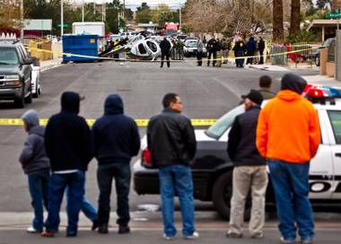 Onlookers watch as crime scene investigators work the scene of a LVMPD helicopter down in the street at 23rd Street north of Bonanza Road after a crash landing on Wednesday, December 31, 2014.