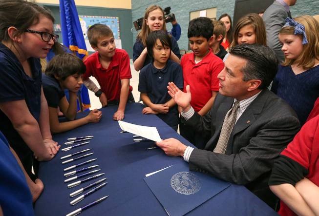 Gov. Brian Sandoval talks with a group of Carson City fifth-graders after signing into law an emergency bill extending bonds for school construction at a brief ceremony in Carson City on Wednesday, March 4, 2015. More than a dozen lawmakers joined Sandoval for the signing of the bill which had bipartisan support in both houses. 