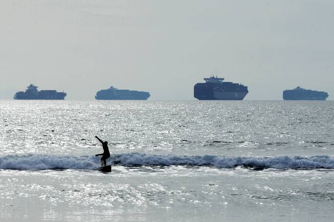 A surfer rides a wave in Sunset Beach, Calif., as loaded cargo ships, with billions of dollars of cargo onboard, are anchored outside the Ports of Long Beach and Los Angeles.