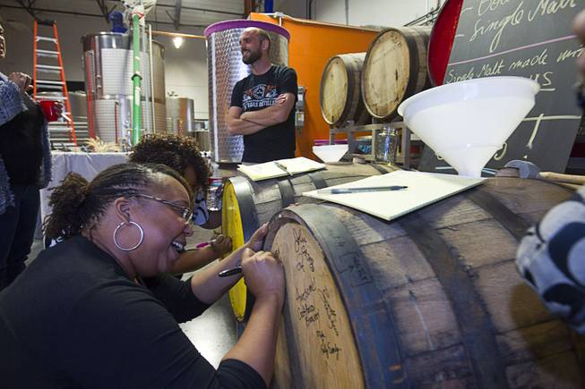 Lauren Spenser, left, of Henderson signs a barrel during the first St. George Day Spring Whiskey Barreling celebration at the Las Vegas Distillery in Henderson Saturday, April 25, 2015. St. George's Day remembers Saint George, England's patron saint. The distillery owner and his son are also named George.