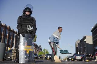 Residents clean streets as law enforcement officers stand guard, Tuesday, April 28, 2015, in Baltimore, in the aftermath of rioting following Monday's funeral of Freddie Gray, who died in police custody. (AP Photo/Matt Rourke)