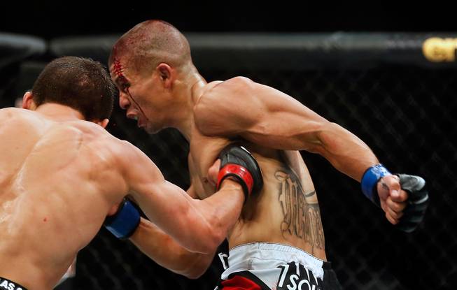 UFC flyweight contender Joseph Benavidez connects with a damaging punch to the ribs of bloodied contender John Moraga working to finish him off during their UFC 187 fight at the MGM Grand Garden Arena on Friday, May 22, 2015.