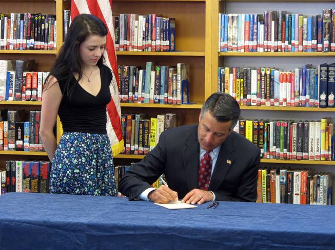 Gov. Brian Sandoval signs into law on Monday, June 8, 2015, a measure creating millions of dollars in incentives to combat the state's teacher shortage as his daughter, Maddy, watches in the library at Reno High School, where she is a senior.
