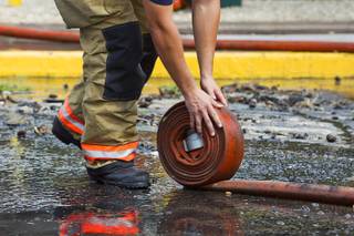 A firefighter rolls up a hose after an early morning three-alarm fire at the Sandpebble Village apartments at Arville Street and Sirius Avenue Sunday, June 28, 2015.