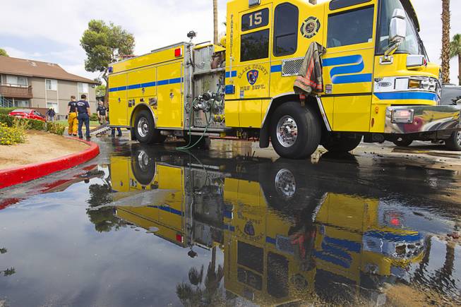 A fire engine is reflected in a puddle after an early morning three-alarm fire at the Sandpebble Village apartments at Arville Street and Sirius Avenue Sunday, June 28, 2015.