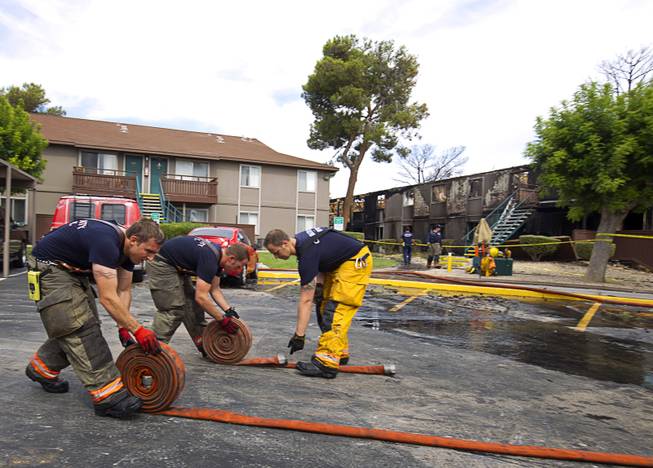 Firefighters roll up hoses after an early morning three-alarm fire at the Sandpebble Village apartments at Arville Street and Sirius Avenue Sunday, June 28, 2015.