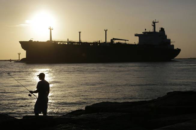 In this July 21, 2015, file photo, an oil tanker passes a fisherman as it enters a channel near Port Aransas, Texas, heading for the Port of Corpus Christi. The price of U.S. crude oil slid Friday, Aug. 21, 2015, to $39.86.