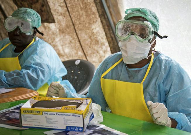 Health workers wearing protective clothing and equipment against the deadly Ebola virus sit in a screening tent Aug. 9, 2014, at the government hospital in Kenema, eastern Sierra Leone. World Health Organization responders were so constrained by bureaucracy that Director-General Dr. Margaret Chan intervened, writing in an Aug. 3, 2014, email that logistics experts in West Africa were getting only a couple hundred dollars a week to cover thousands of dollars in expenses for basics like protective rubber boots and disinfectant.