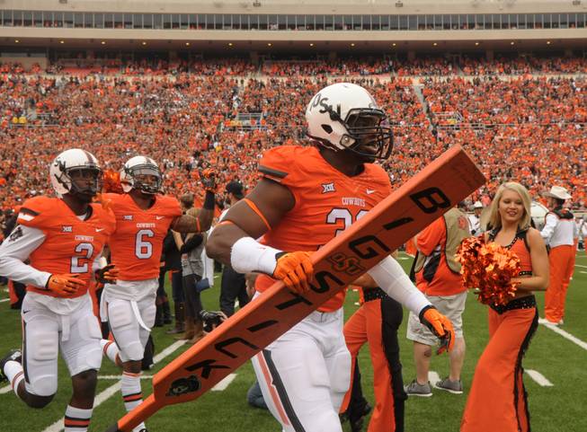 Oklahoma State defensive end Emmanuel Ogbah (38) carries the team's "Big Stick" onto the field at the start of an NCAA college football game between Kansas and Oklahoma St in Stillwater, Okla., Saturday, Oct. 24, 2015.