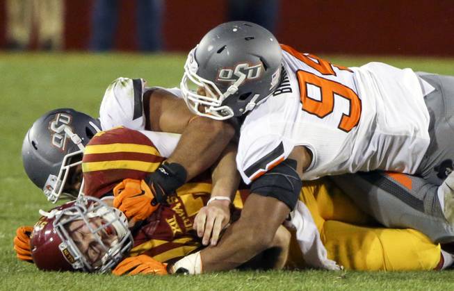 Oklahoma State defensive tackle Eric Davis, back left, and defensive end Jordan Brailford, right, tackle Iowa State quarterback Joel Lanning, front left, during the second half of an NCAA college football game, Saturday, Nov. 14, 2015, in Ames, Iowa.