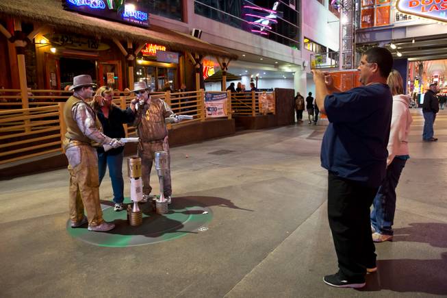 From left, Dennis Patterson and Chad Fritz, living silver statues, pose with a tourist on the Fremont Street Experience, Tuesday Nov. 17, 2015. A new regulation takes effect today that brings order to the chaos of street performers.