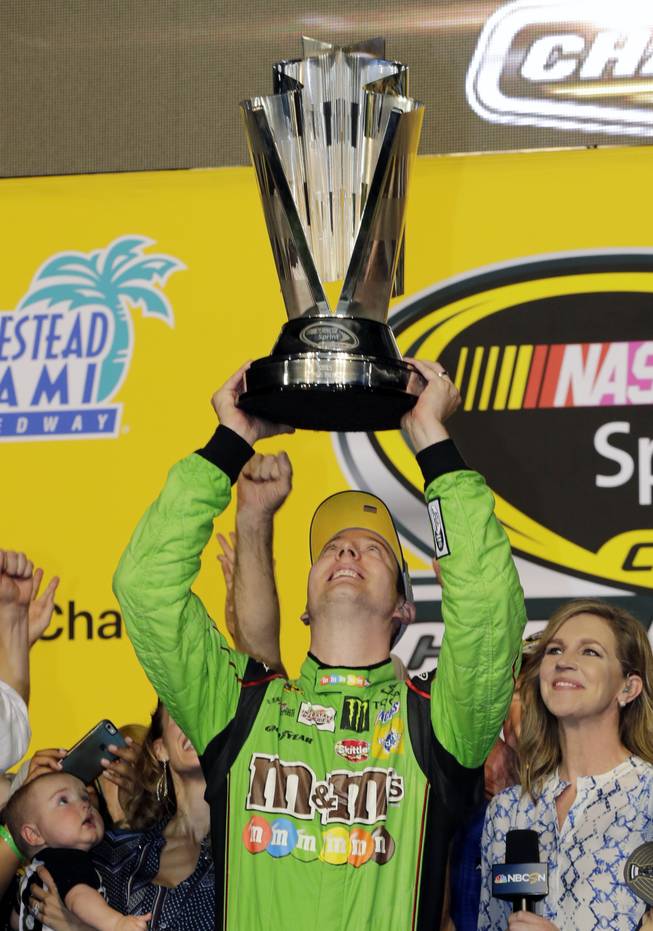 Kyle Busch raises his trophy after winning the NASCAR Sprint Cup Series auto race and the season title Sunday, Nov. 22, 2015, at Homestead-Miami Speedway in Homestead, Fla.