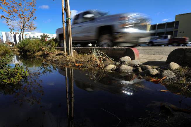 Cars drive on Woodman Avenue in Panorama City, Calif., Thursday, Jan. 7, 2016, beside a culvert where rainwater runoff is directed to a leach field on the side of the street. With California entering what may be a fifth year of drought, water agencies are moving to capture and store more water. 