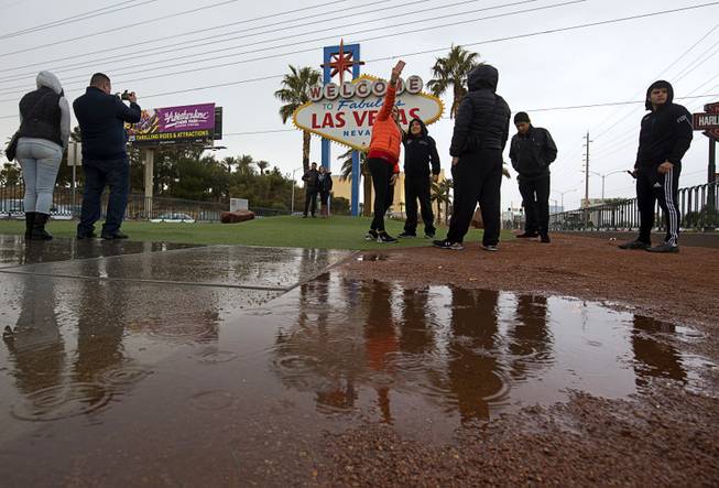 Tourists brave rainy weather to take photos in front of the "Welcome to Las Vegas" sign Sunday, Jan. 31, 2016.  