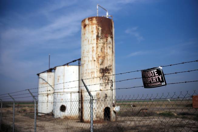 A private property sign hangs Jan. 15, 2015, on the fence of a shut-down injection well next to an almond orchard owned by Palla Farms in Bakersfield, Calif. Palla Farms filed suite blaming several oil companies for contaminating the local groundwater and killing cherry trees.