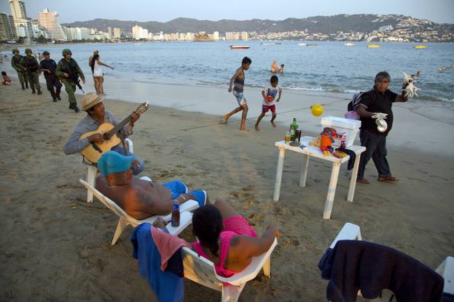 A roving seashell vendor walks past as a street musician serenades a local couple and Marines and local police patrol the shore Wednesday, May 11, 2016, of Papagayo Beach in Acapulco, Mexico.