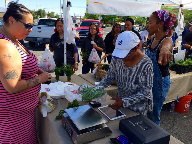 Geneva Ruiz, left, waits as a volunteer rings up her produce purchases at the Veggie Buck Truck, a  mobile farmer's market that debuted Friday, June 3, 2016.  Its first stop was a Nevada Welfare Division office on Belrose Street. Rosalind Brooks, right, who is the founder of Vegas Roots community garden, which created the Veggie Buck Truck, points to a register for waiting customers.