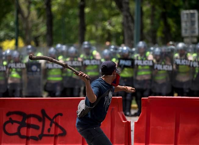 A student aims a stick of wood at Bolivarian National Police officers during clashes outside the Central University in Caracas, Venezuela, Thursday, June 9, 2016. Students had planned to march from Venezuela's top university to elections headquarters, but hundreds of police in riot gear blocked the way. Students covered their faces with Venezuelan flags and threw bottles, stones and sticks while police lobbed tear gas. 