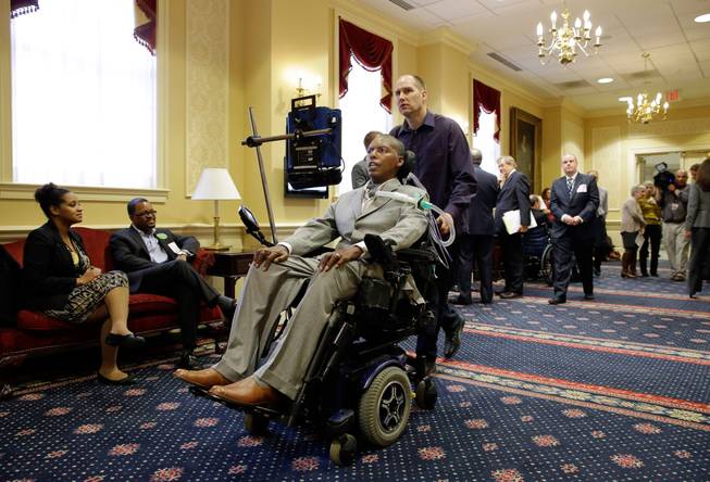 O.J. Brigance, a former Baltimore Ravens football player and current senior advisor to player development, is pushed March 10, 2015, by a nurse whose name was only given as Bill outside a committee room after testifying to Maryland lawmakers against a right-to-die bill in Annapolis, Md. Brigance will take his personal fight against ALS to the baseball diamond on the 77th anniversary of Lou Gehrig’s farewell speech at Yankee Stadium. Brigance will honor the former Yankees first baseman by participating in the traditional first-pitch ceremony Monday, July 4, 2016, at the home of the Class A Aberdeen IronBirds.