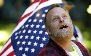 A protester carries an upside down American flag as he looks up at the federal courthouse in Portland, Ore., Tuesday, Sept. 13, 2016.  Opening statements are set to begin Tuesday in the trial of the Bundy brothers, Ammon and Ryan, and five others who occupied a remote bird sanctuary in Oregon's high desert early this year. The standoff drew national attention to the decades-old fight between the federal government and Western states over land policy.  (AP Photo/Don Ryan)