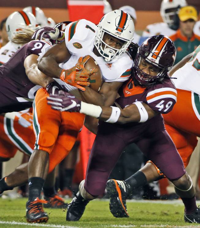 Miami running back Mark Walton (1) tries to get past Virginia Tech linebacker Tremaine Edmunds (49) and defensive lineman Vinny Mihota, left, during the first half of an NCAA college football game at Lane stadium in Blacksburg, Va., Thursday, Oct. 20, 2016. 