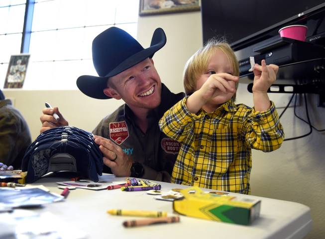 Saddle bronc world champion Jacobs Crawley, left, sits with Tristan Duenez, 3, during a visit to the Grant a Gift Autism Foundation at the UNLV Medicine Ackerman Autism Center Friday, Dec. 2, 2016, in Las Vegas.