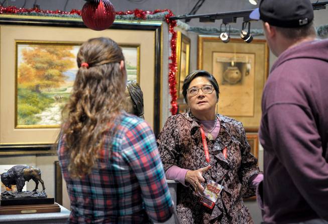 Risa Franco, center, of Dumas, Tex., talks with visitors about her husband M.S. Franco's western art at the NFR Cowboy Christmas gift show in the South Halls of the Las Vegas Convention Center on Thursday, Dec. 1, 2016.  With just under 350 exhibitors from across the United States and Canada, the Cowboy Christmas features unique products, including custom-jewelry, western wear, boots and spurs, furniture, original art, handmade crafts and home goods.