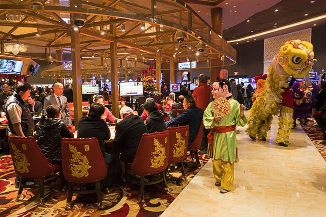 A performer and dragon dancers pass by table game gamblers at Lucky Dragon during the boutique casinos grand opening celebration, Saturday, Dec. 3, 2016.