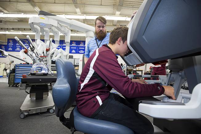 Clint Barnes, manufacturing instructor at Cimarron-Memorial High School, looks on as sophomore Dustan Wile tries out Intuitive's da Vinci Xi robotic surgical system at the school's engineering lab Tuesday, Dec. 6, 2016. MountainView Hospital and Intuitive Surgical, Inc. partnered in the event to teach students about careers in robotics, engineering and medicine.