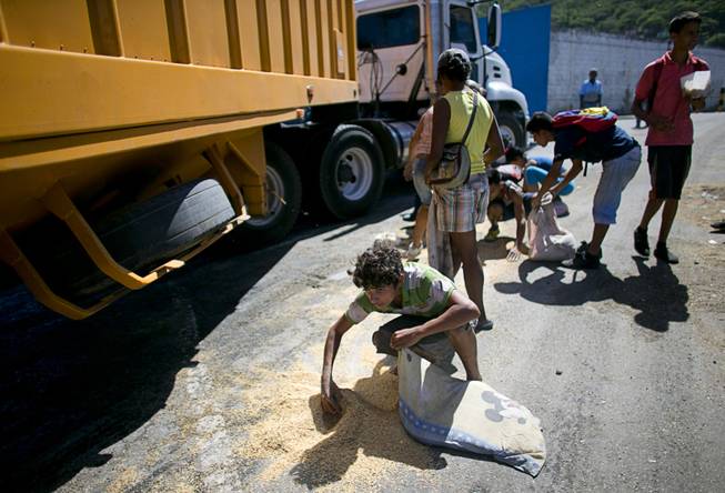 In this Nov. 14, 2016 photo, a youth uses his pillow as a bag to collect rice from the pavement that shook loose from a food cargo truck waiting to enter the port in Puerto Cabello, Venezuela, the port that handles the majority of Venezuela's food imports. As millions of Venezuelans go hungry this year, food trafficking has become one of the most lucrative businesses in the country.