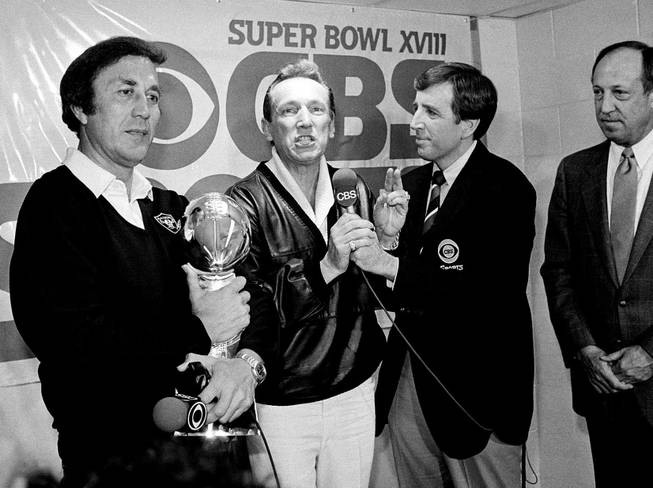 In this Jan. 23, 1984, file photo, Oakland Raiders coach Tom Flores clutches the Super Bowl trophy as Raiders managing general partner Al Davis is interviewed by Brent Musburger in the locker room after their 38-9 win over the Washington Redskins in Super Bowl XVIII in Tampa, Fla. At right is NFL Commissioner Pete Rozelle.