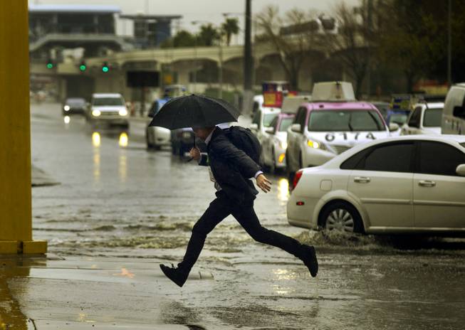 A pedestrian leaps over water onto the sidewalk along E. Elvis Presley Blvd. as rain soaks the Las Vegas valley on Tuesday, Jan. 9, 2018.