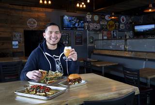 Van-Alan Nguyen, owner of 595 Craft and Kitchen and Art District Kitchen, poses with a Pork Belly Banh Mi and a glass of Beachwood Brewing's 