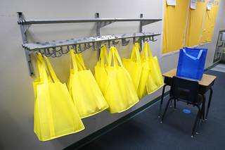 Bags of school supplies hang from a rack at Petersen Elementary School Wednesday, Feb. 24, 2021. Blue bags have school supplies for one group of students. Students that come on different days will have yellow bags.