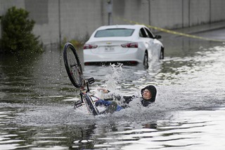 A cyclist falls while trying to ride through floodwaters near a stranded car, Friday, Sept. 1, 2023, in Las Vegas.
