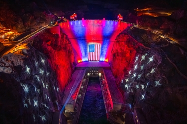 A 300-foot-wide, 150-foot-tall American flag now hangs across the face of Hoover Dam, illuminated by patriotic lighting in red, white and blue — what officials are calling ....