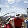 Tourists walk on the sidewalk along the Hoover Dam, with construction of the dam bypass bridge seen in the background Friday, Feb. 26, 2010.