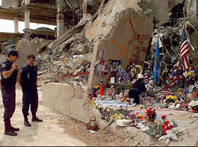Officials stand near the Alfred P. Murrah Federal Building in Oklahoma City, Friday, May 5, 1995, as workers place flowers and memorial items at the scene fo the April 19, deadly car-bombing. The memorial items came from a makeshift memorial which had been built by mourners blocks away from the bomb site.  Rescue crews ended their search for victims Thursday, with two bodies still missing. 