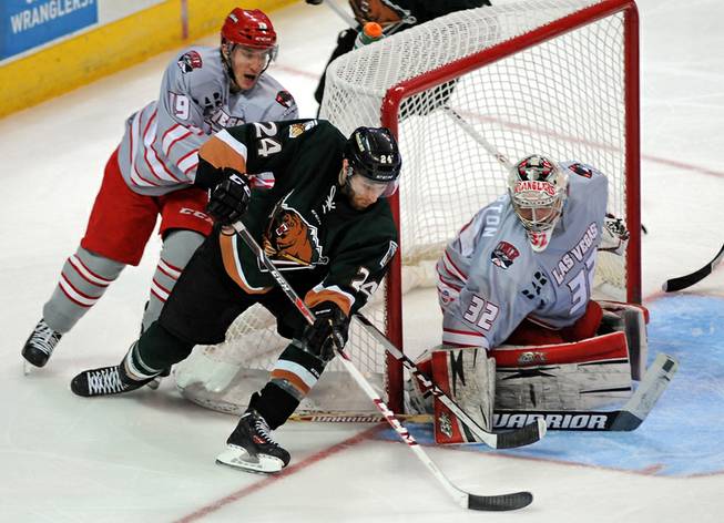 Utah Grizzlies defenseman Martin Lee attempts a backhanded wrap around shot as Wranglers goaltender Travis Fullerton covers the corner of the net during the second period of play on Friday night. Wrangler forward Adam Hughesman is defending on the play behind the net.