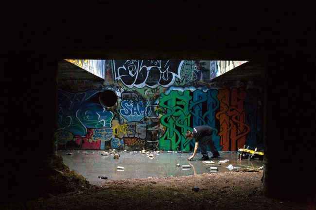 Graffiti artist Ruckoh reaches for a can of spray paint in a pool of water in a storm drain lit by a street grate almost directly under the Las Vegas Strip. 