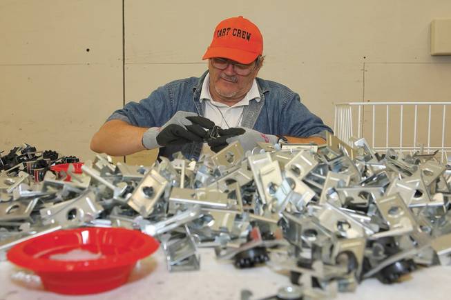 Charles Bender III works through a pile of metal and rubber pieces, constructing sound-isolation inserts for a large-quantity fulfillment contract for Pack International at Opportunity Village.