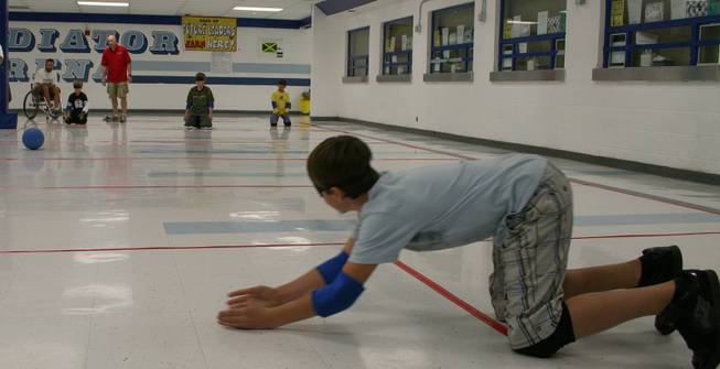 A little boy lays out to stop the rolling ball in goal ball, a game specifically designed for the visually impaired where the ball has a bell in it to hear and the boundaries are strings covered in tape so that players know where the goals are by touch. The boy is actually visually-able, but is wearing an eye mask to block him from seeing.