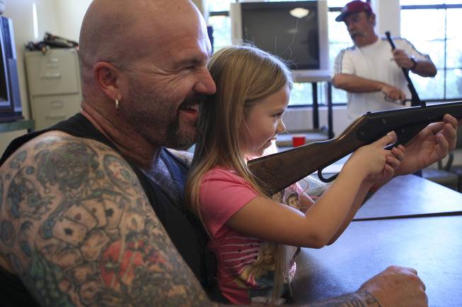 Sitting on the lap of her dad, Ryan Allain, first-grader Brooke Davis gets a shooting lesson while competing for the first time Tuesday in the annual Turkey Shoot at the Boulder City Recreation Center.
