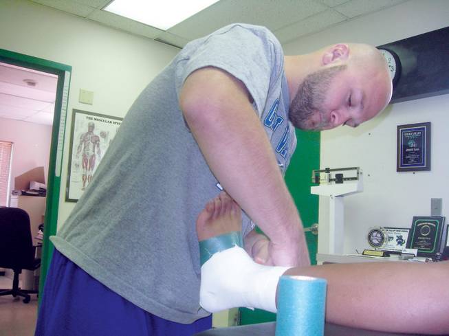 Green Valley High athletic trainer, Jeremy Haas, wraps the foot of senior defensive end Derrick Garrett.