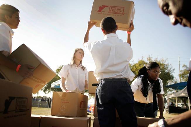 House of Knowledge Christian Academy students, from left, Kyle Jackson, 15; Justine Scott, 17; Terry McDowell, 14; and Dominique Barker, 15, and volunteer Timothy Barbar, far right, load boxes of food onto tables during an event Monday at Doolittle Park for families in need. More than 1,500 people accepted donations, organizers said.