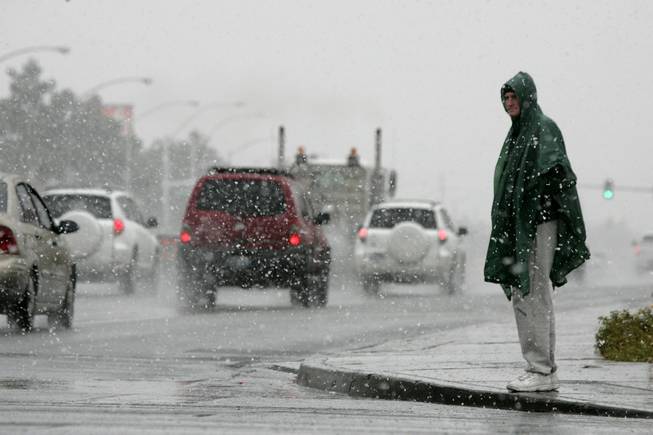 A pedestrian waits for a signal during a snowstorm near ...