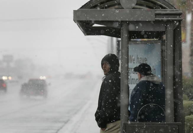 Bus riders wait at a shelter during a snowstorm near ...