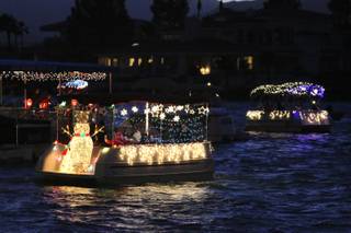 Electric boats decorated with twinkling lights and holiday themes cruise the choppy waters along the shoreline at The Lakes Town Center Plaza during the annual Electric Light Boat Parade Saturday.